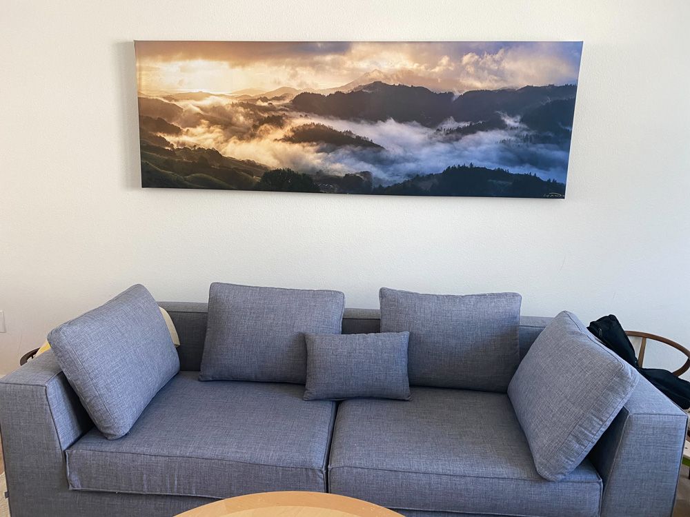 Modern grey sofa with dramatic mountain landscape canvas print mounted on white wall.