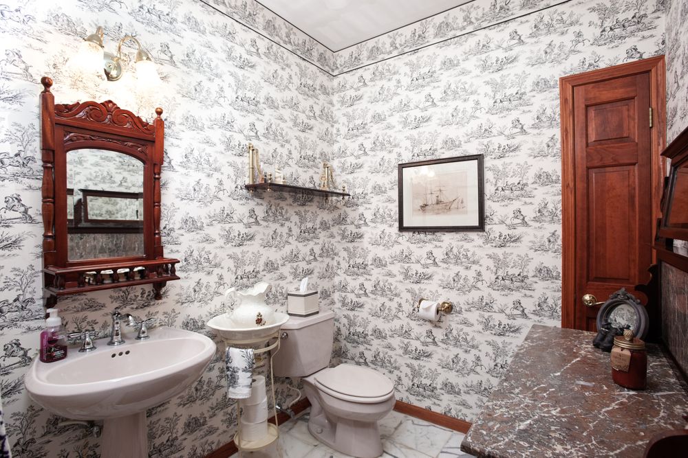 Elegant bathroom featuring black and white toile wallpaper, wooden accents, and classic fixtures.