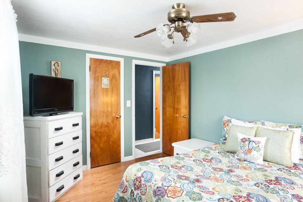Spacious bedroom with mint green walls, white furniture, and floral bedding under a ceiling fan.