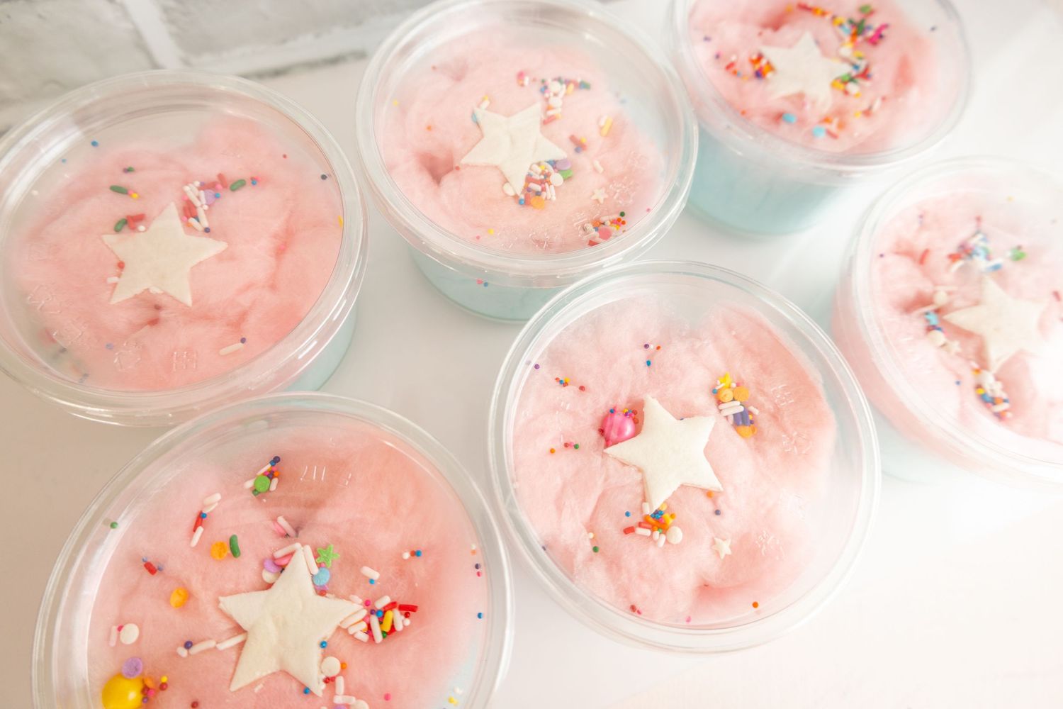 Pink frosted cupcakes with sprinkles arranged in rows on a white surface.