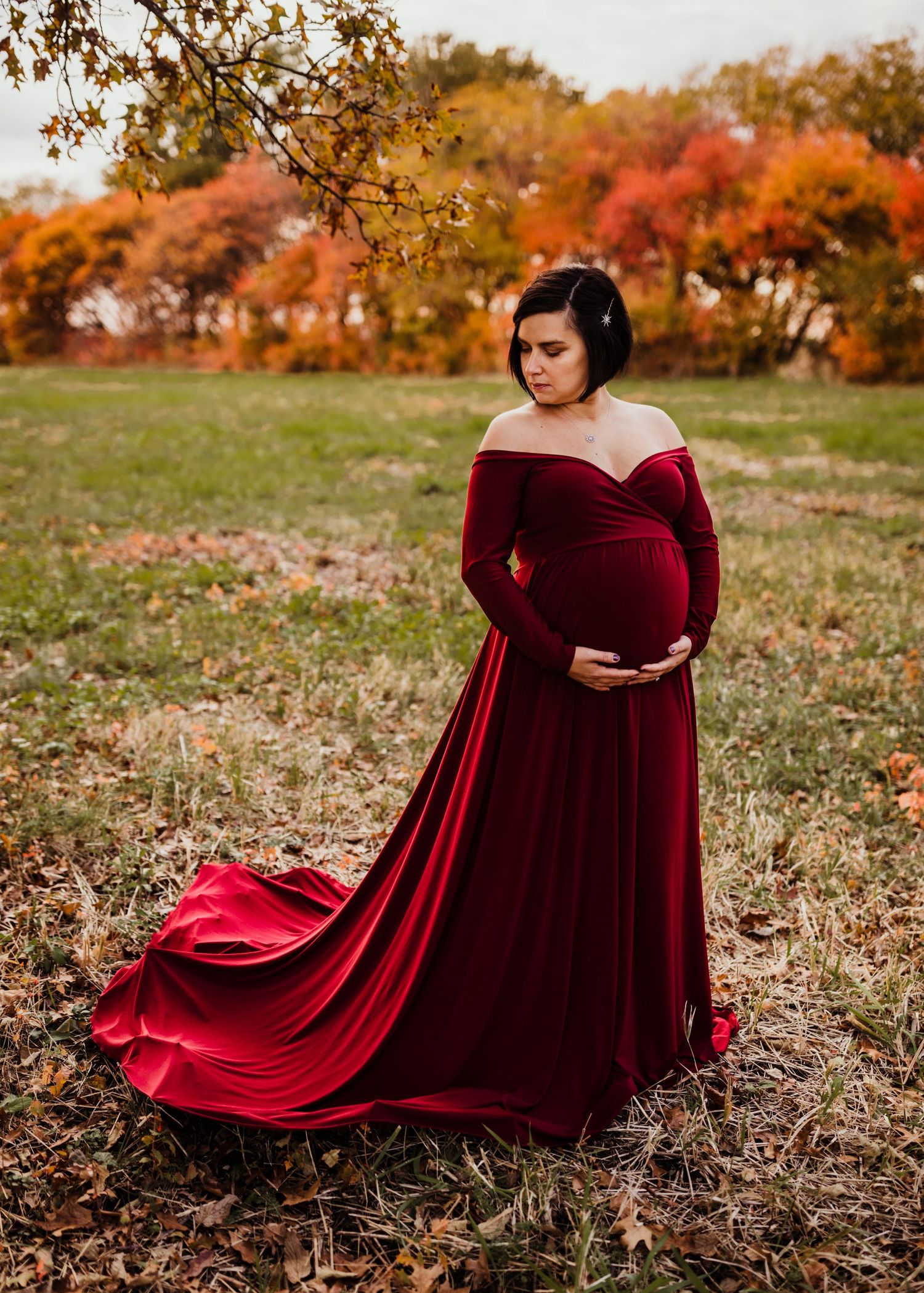 Person in burgundy velvet dress poses dramatically in autumn field.