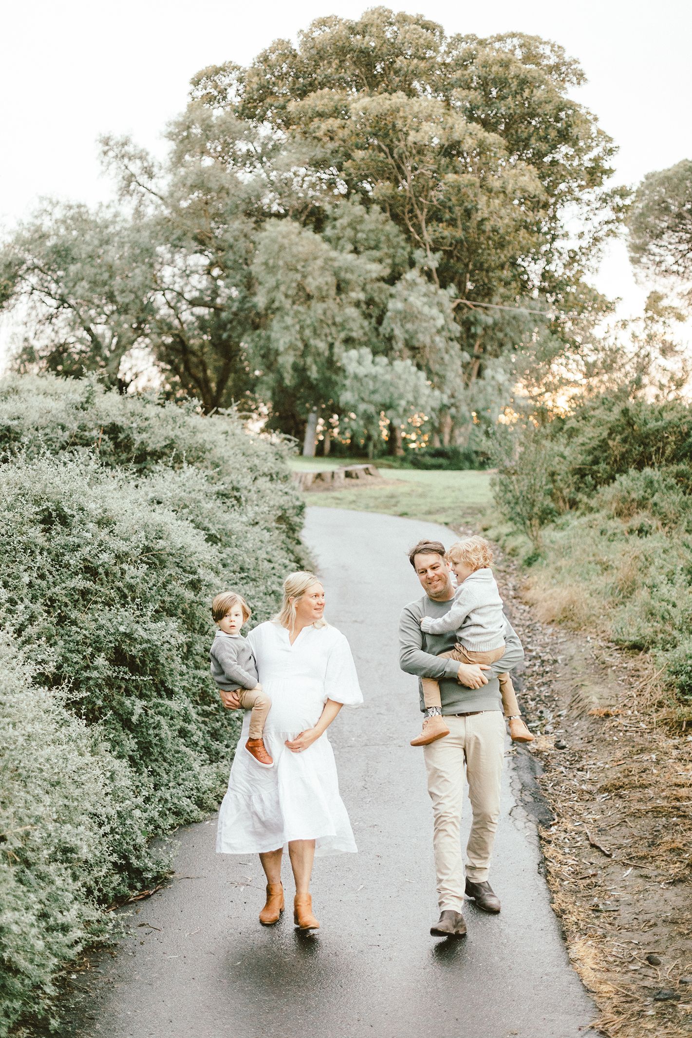 A family takes an evening stroll along a tree-lined path in soft lighting.