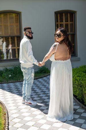 A couple in wedding attire holds hands while walking on a checkered pathway.