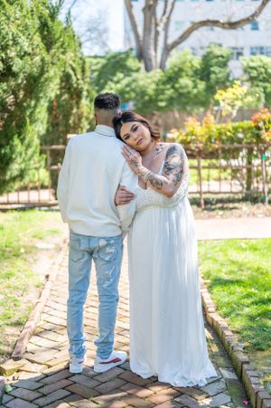 Couple in white embracing on a brick pathway surrounded by lush garden scenery.