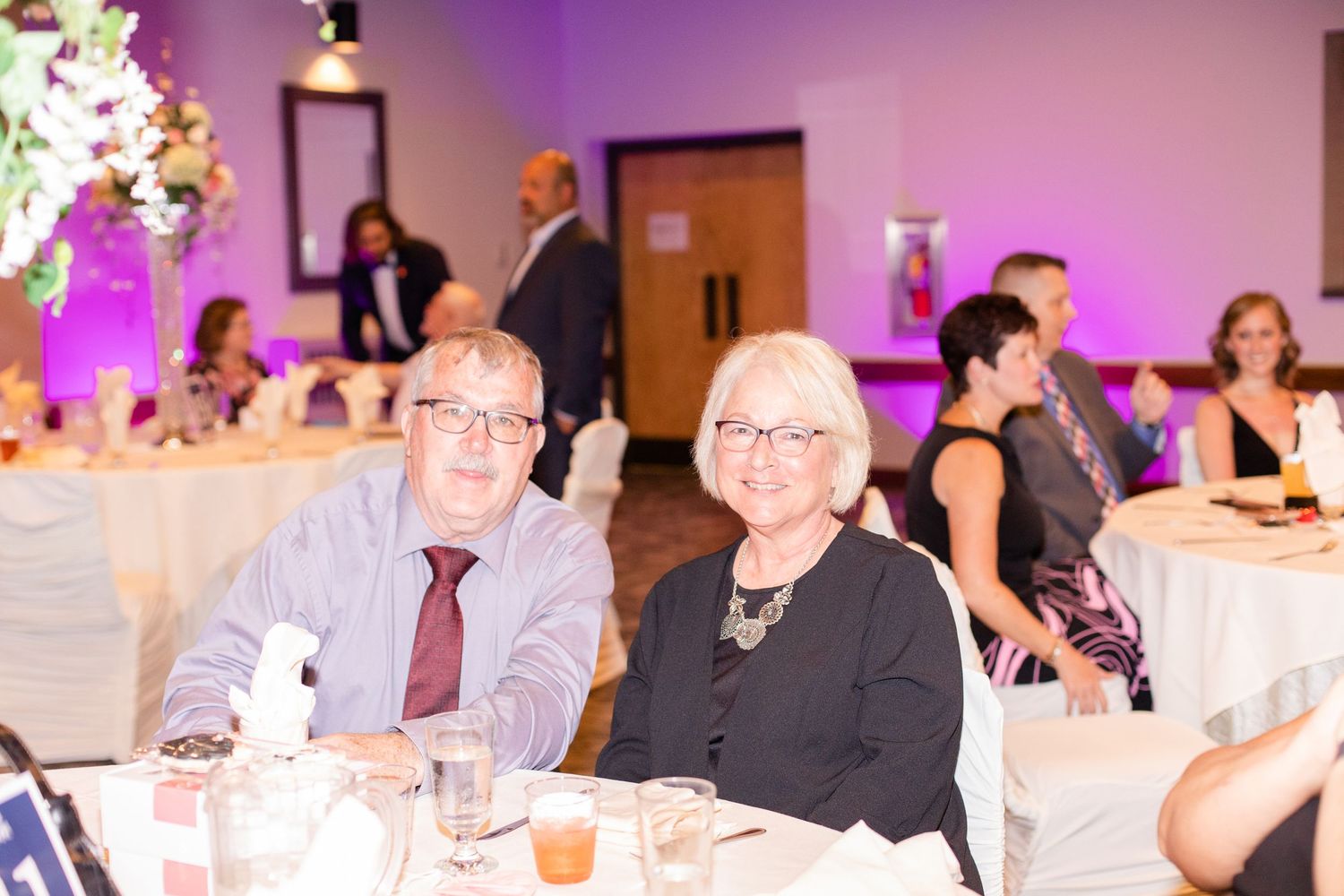 Wedding reception hall with purple ambient lighting and guests seated at decorated tables.