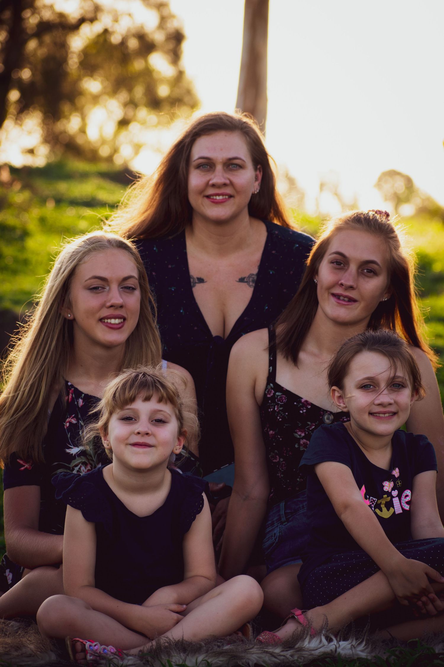 Group portrait of five people in dark clothing sitting together outdoors at sunset.