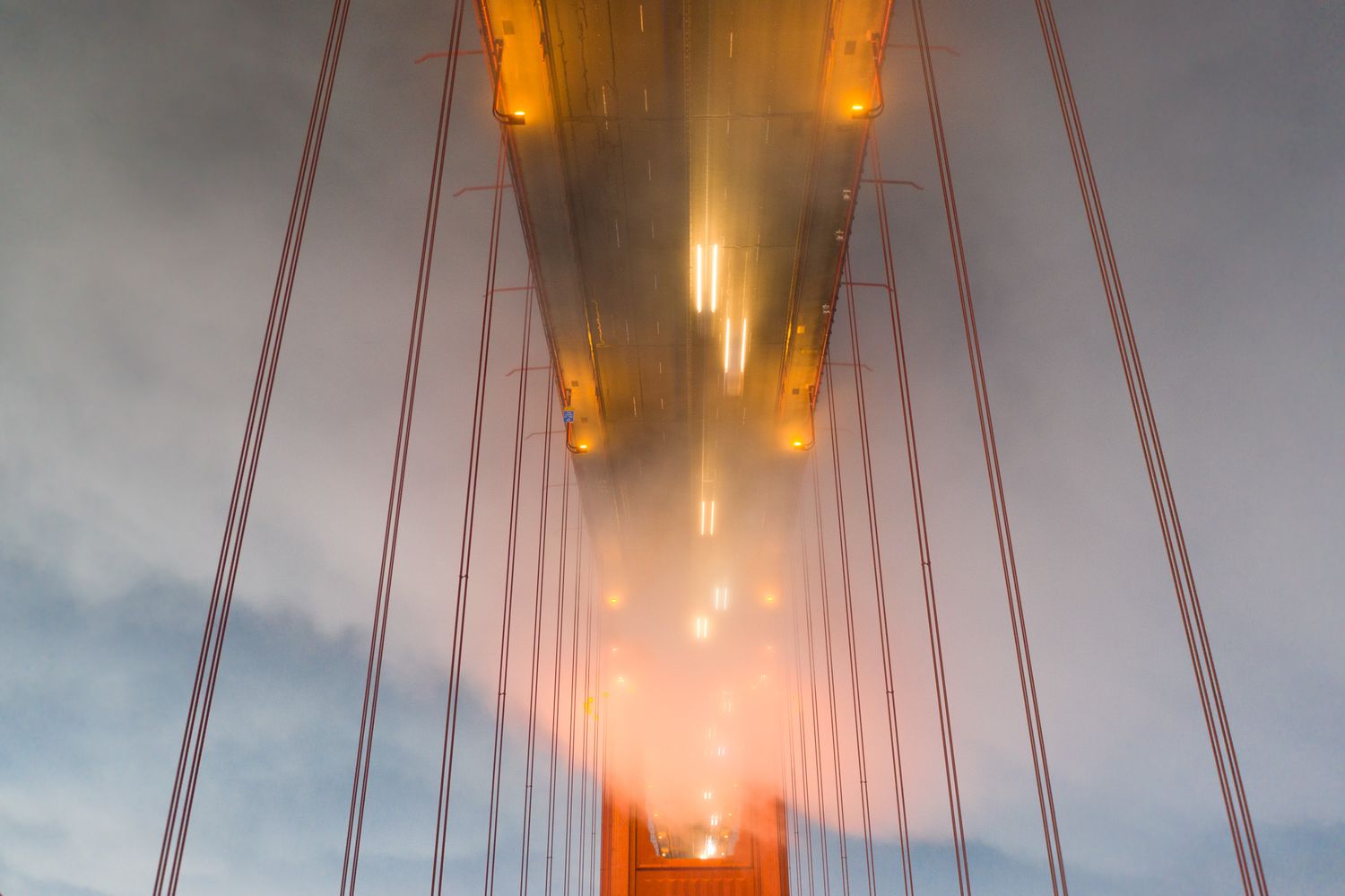 Foggy Golden Gate Bridge towers illuminated in warm orange lights stretching into misty evening sky.