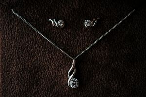 Delicate silver jewelry set with necklace and earrings displayed on dark textured background.