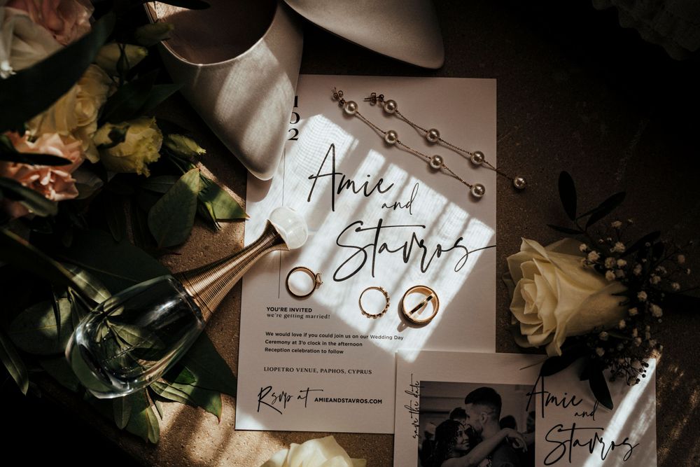 An elegant wedding invitation surrounded by flowers and rings in moody lighting.