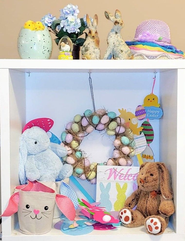 Easter themed shelf display with stuffed animals, flowers, and decorative items in pastel colors.