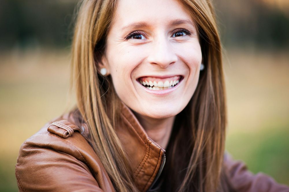 Close-up outdoor portrait showing genuine smile while wearing brown leather jacket.