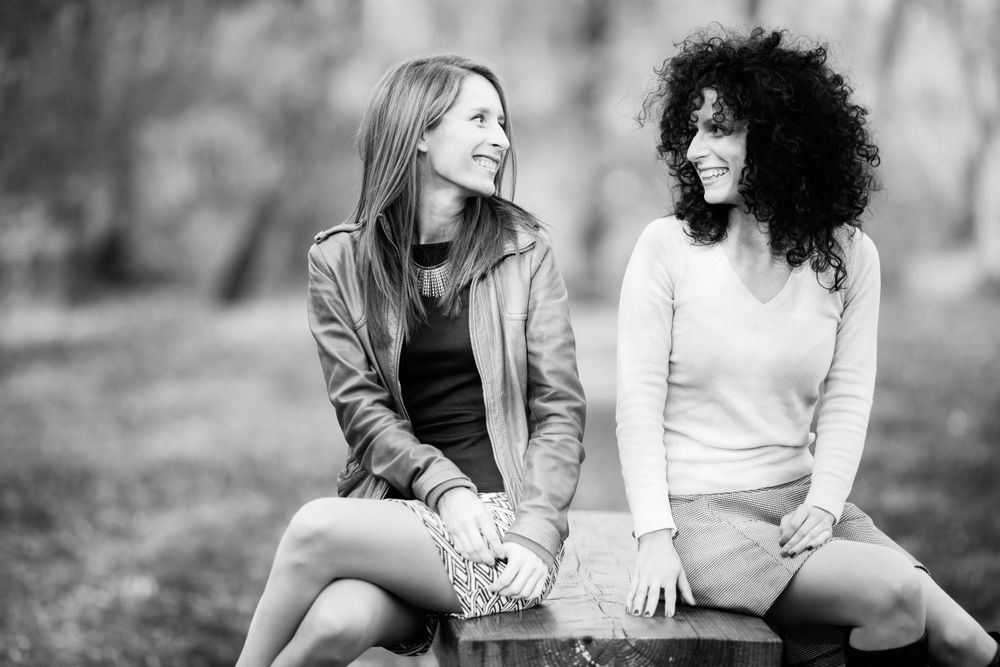 Two friends sitting together outdoors in casual wear having a conversation.