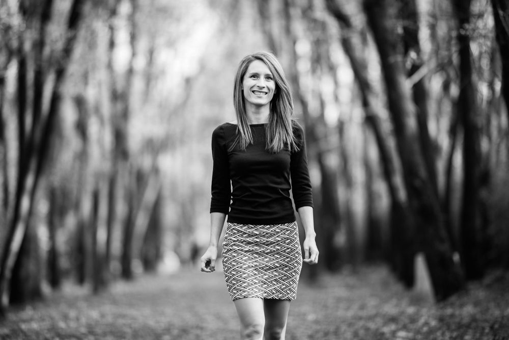 Black and white portrait of person in patterned skirt walking down tree-lined path.