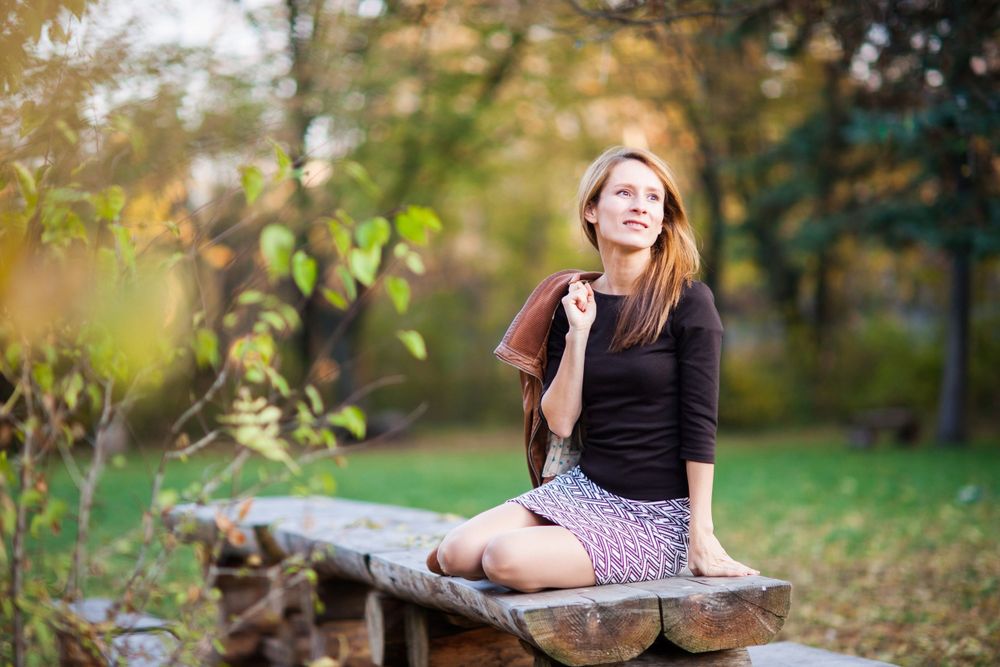 Person sitting on wooden bench in autumn garden setting wearing casual outfit.