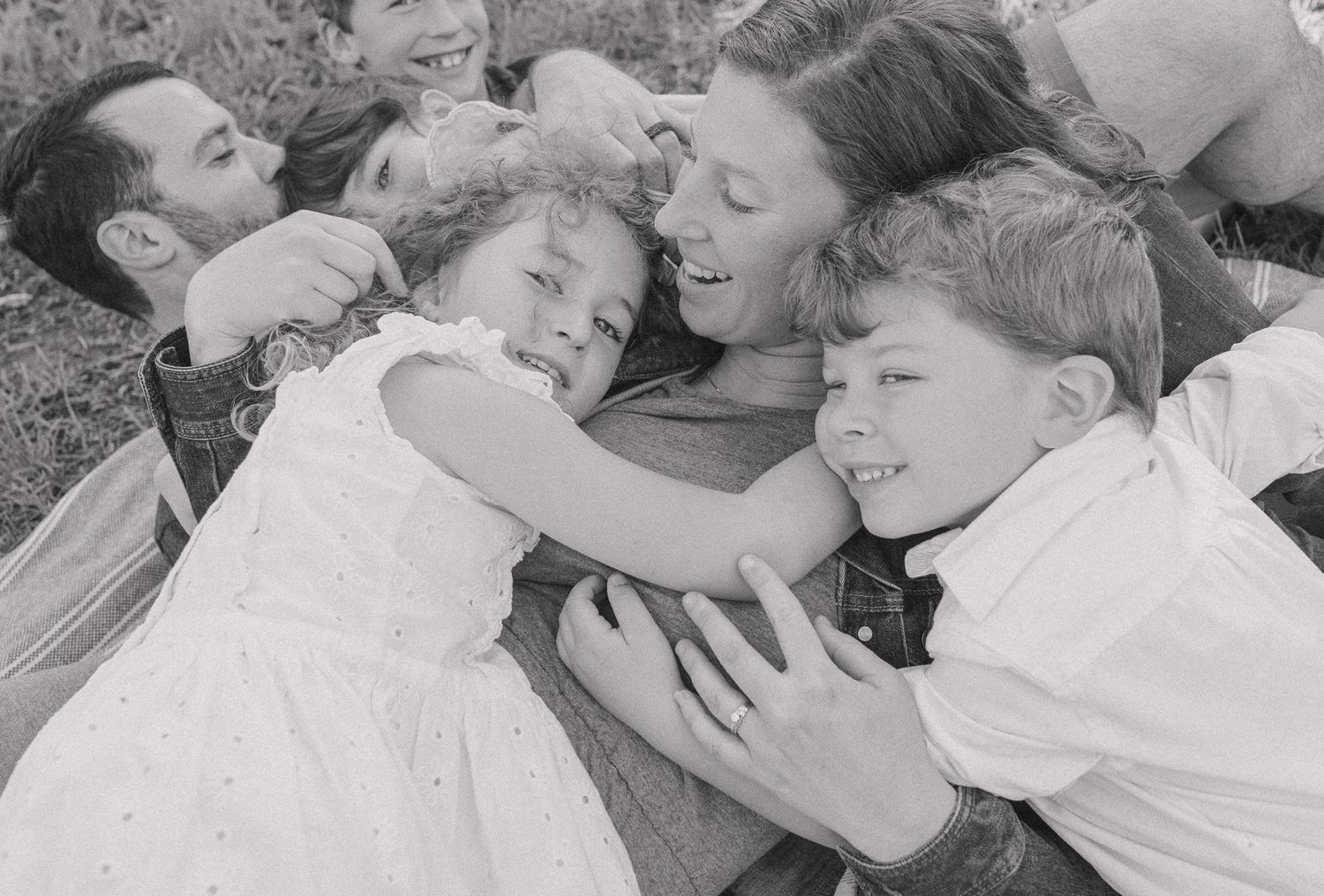 Black and white photo of a joyful family laughing and cuddling together on the grass outdoors.