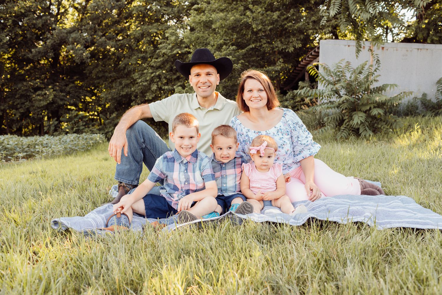 Happy family of five sitting on blanket in green grass for outdoor portrait.