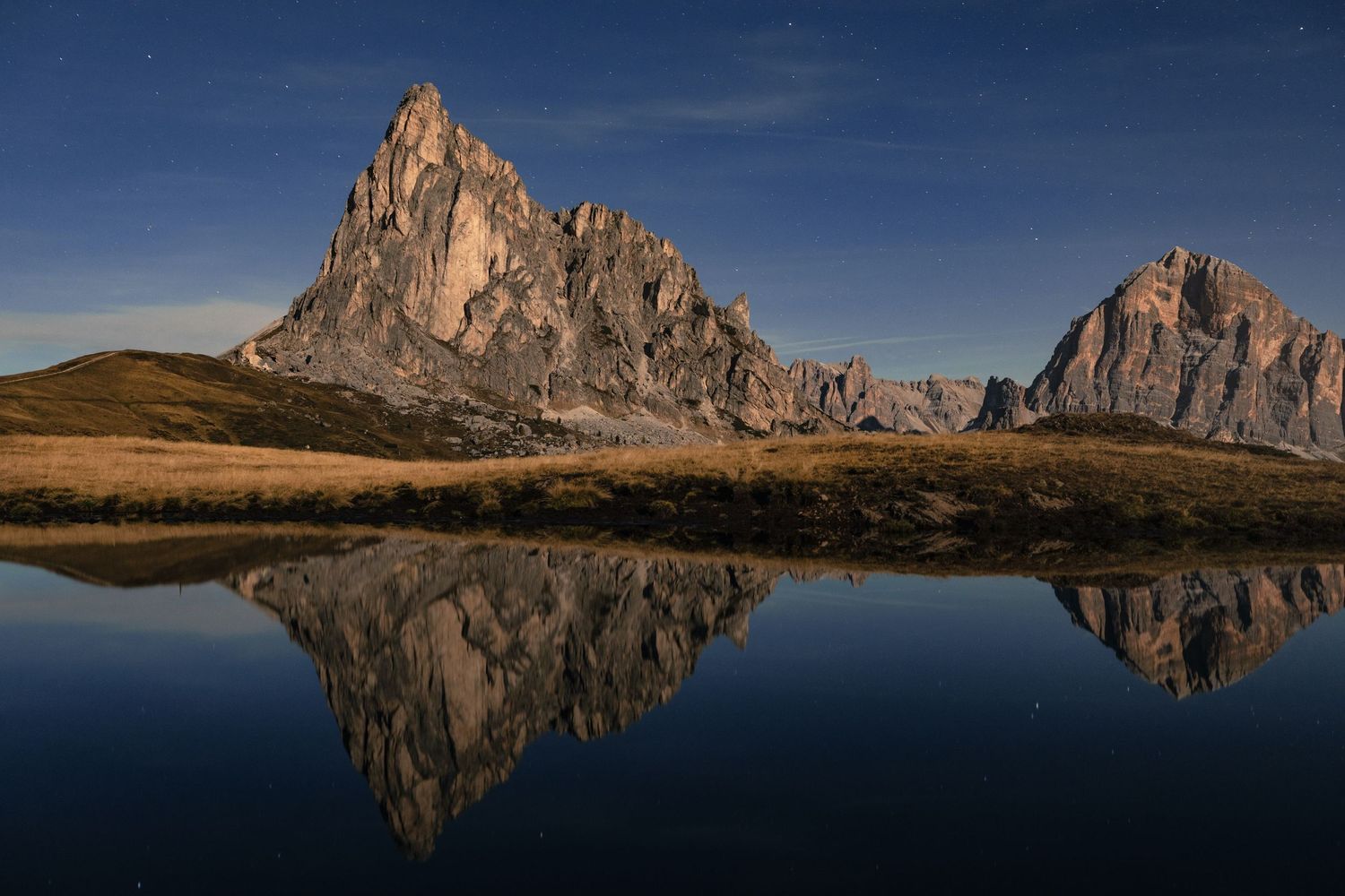 Dramatic mountain peak reflects perfectly in still alpine lake during golden hour.