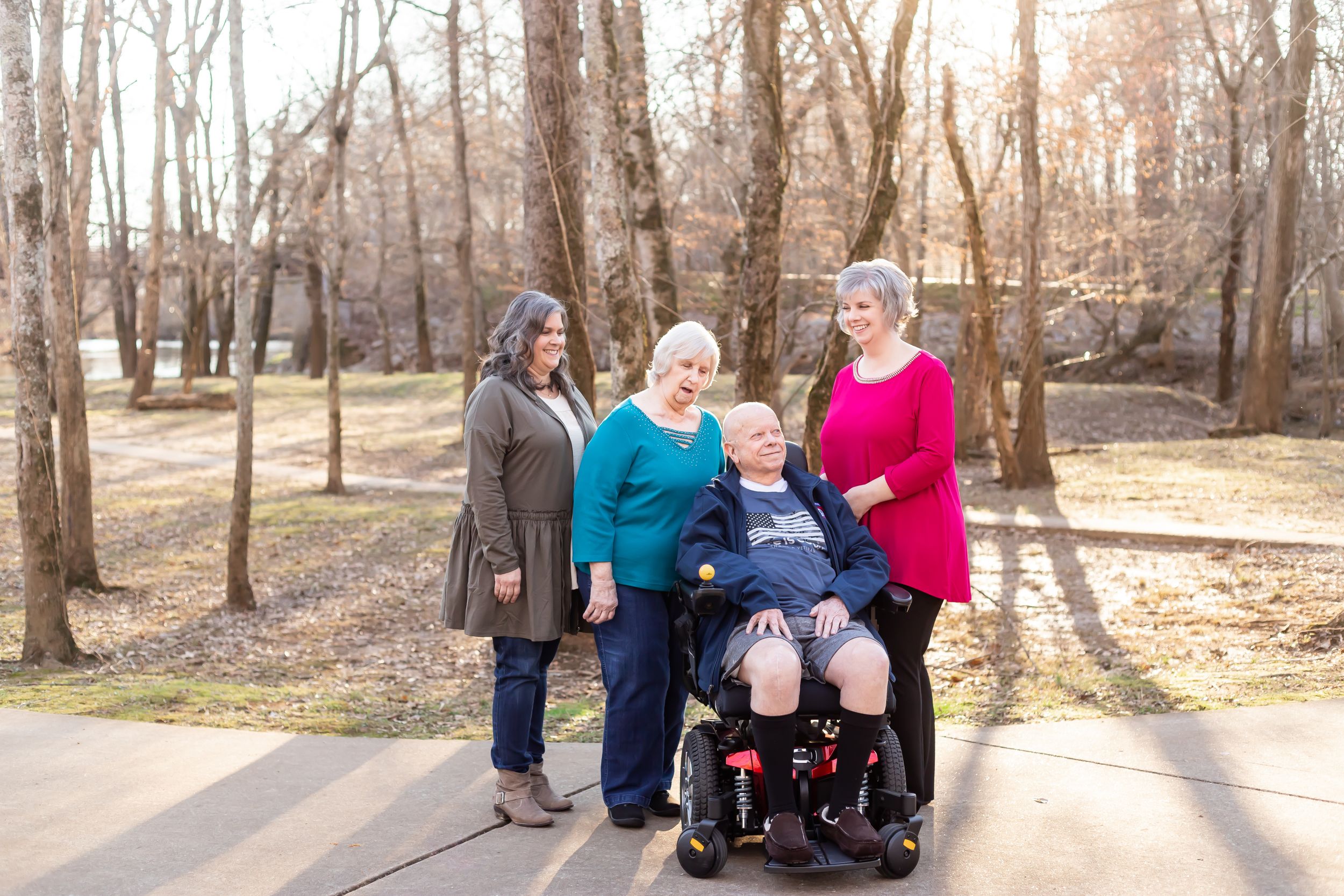 Four people pose together outside on a walking path surrounded by bare winter trees.