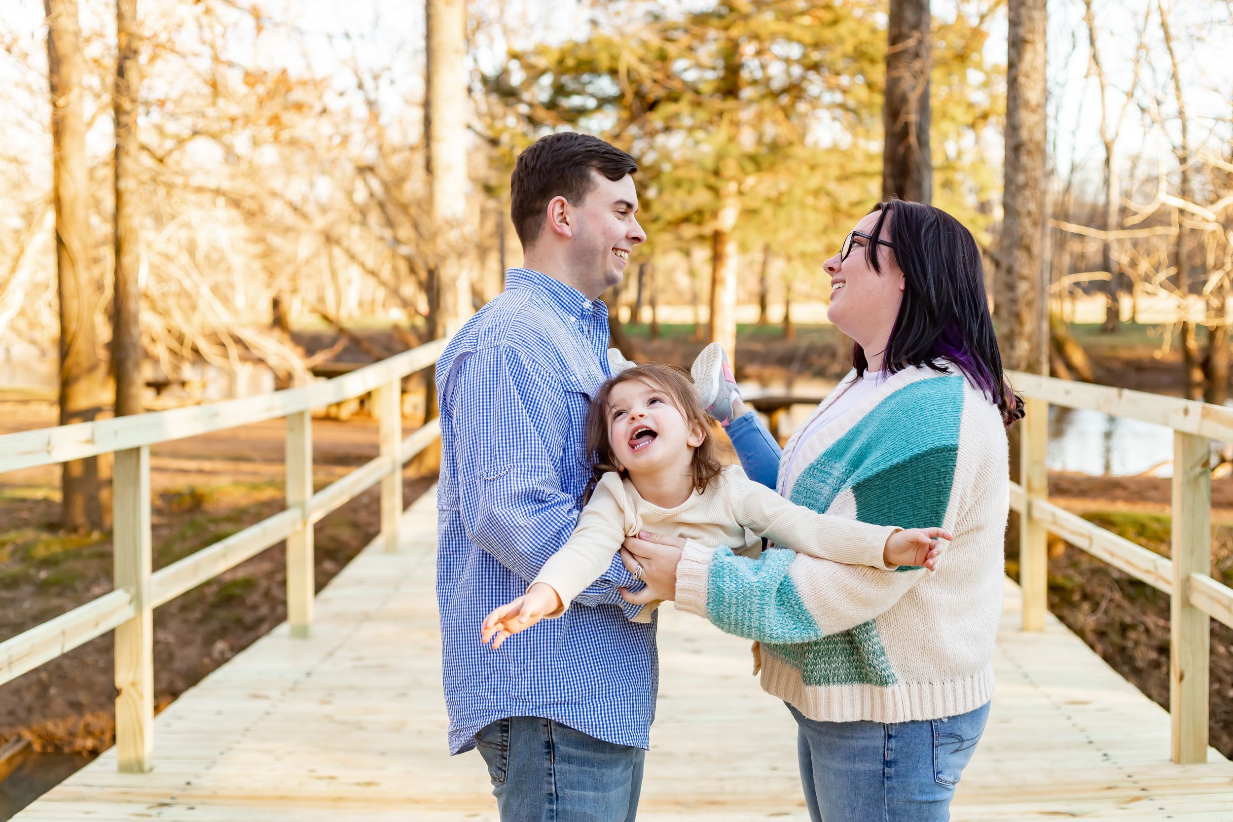 A joyful moment shared between three people on a wooden bridge surrounded by autumn foliage.