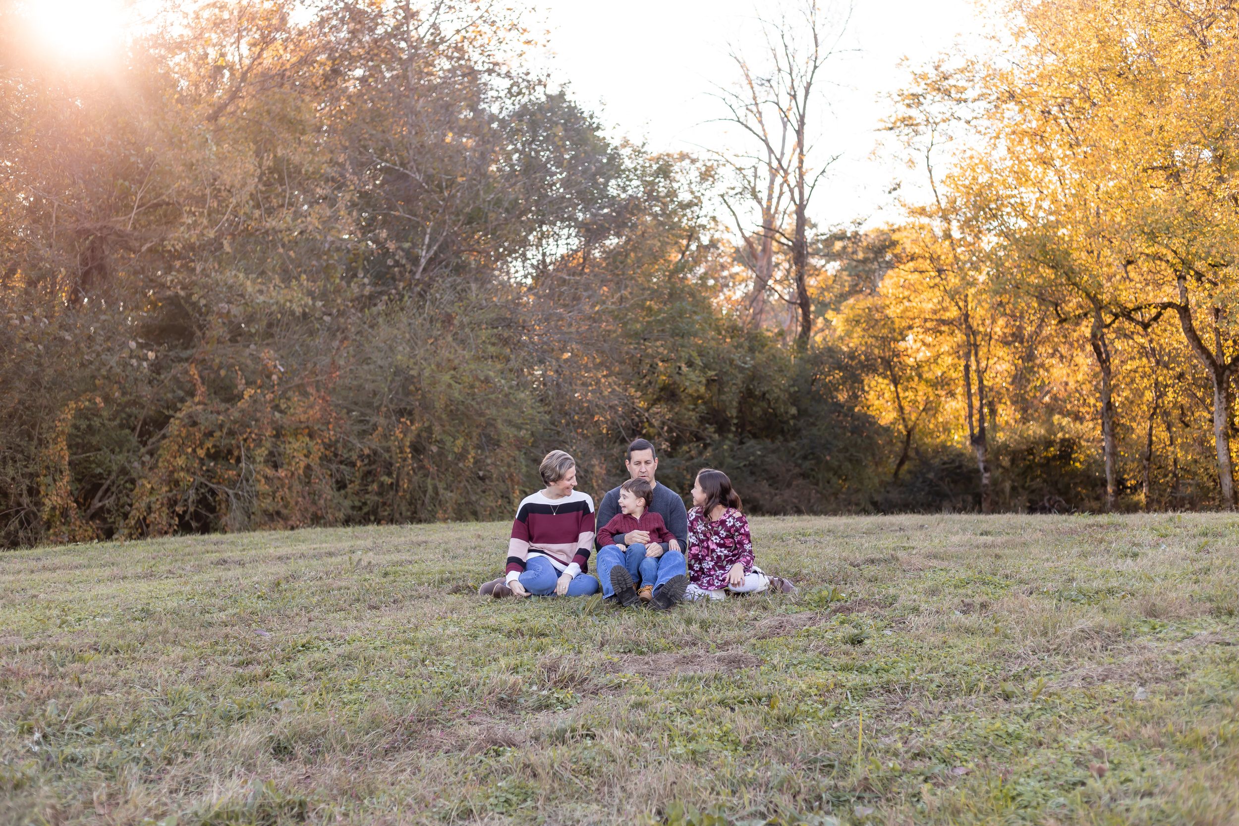 Small group sitting on grass at sunset with golden autumn trees in the background.