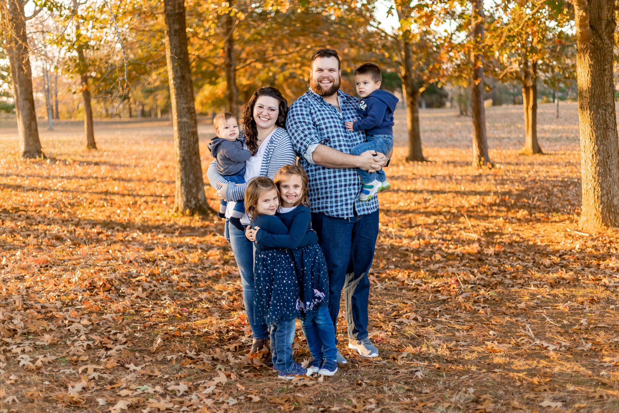 Group portrait in autumn park with fallen orange leaves covering the ground.