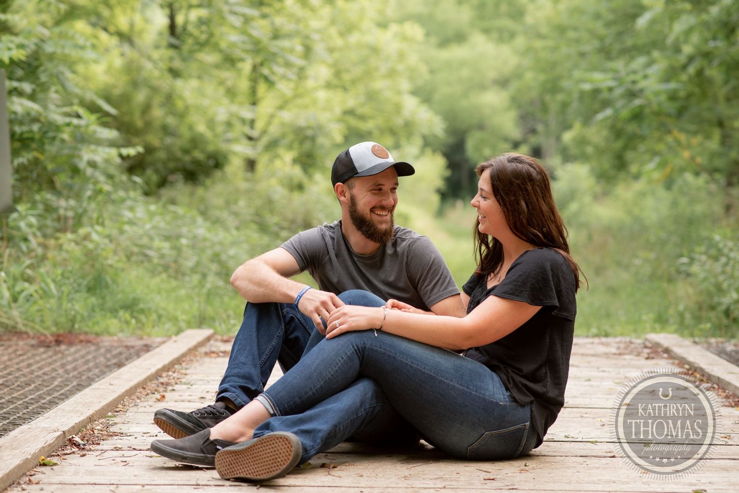 A couple sits together on rustic wooden railroad tracks surrounded by greenery.