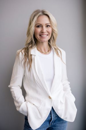 Woman wearing white top and jacket over jeans smiling at the camera