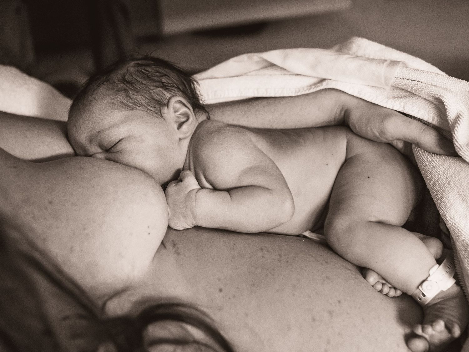 A peaceful newborn baby sleeping skin-to-skin in black and white photography.