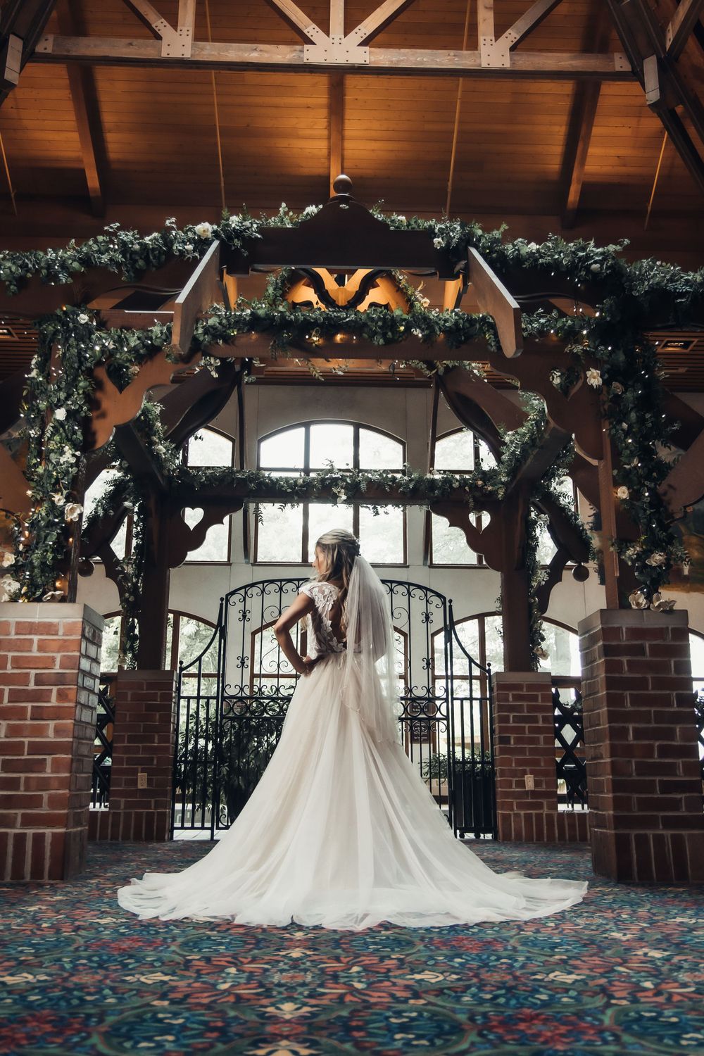 Elegant bridal portrait under a decorated wooden archway with greenery and lights.
