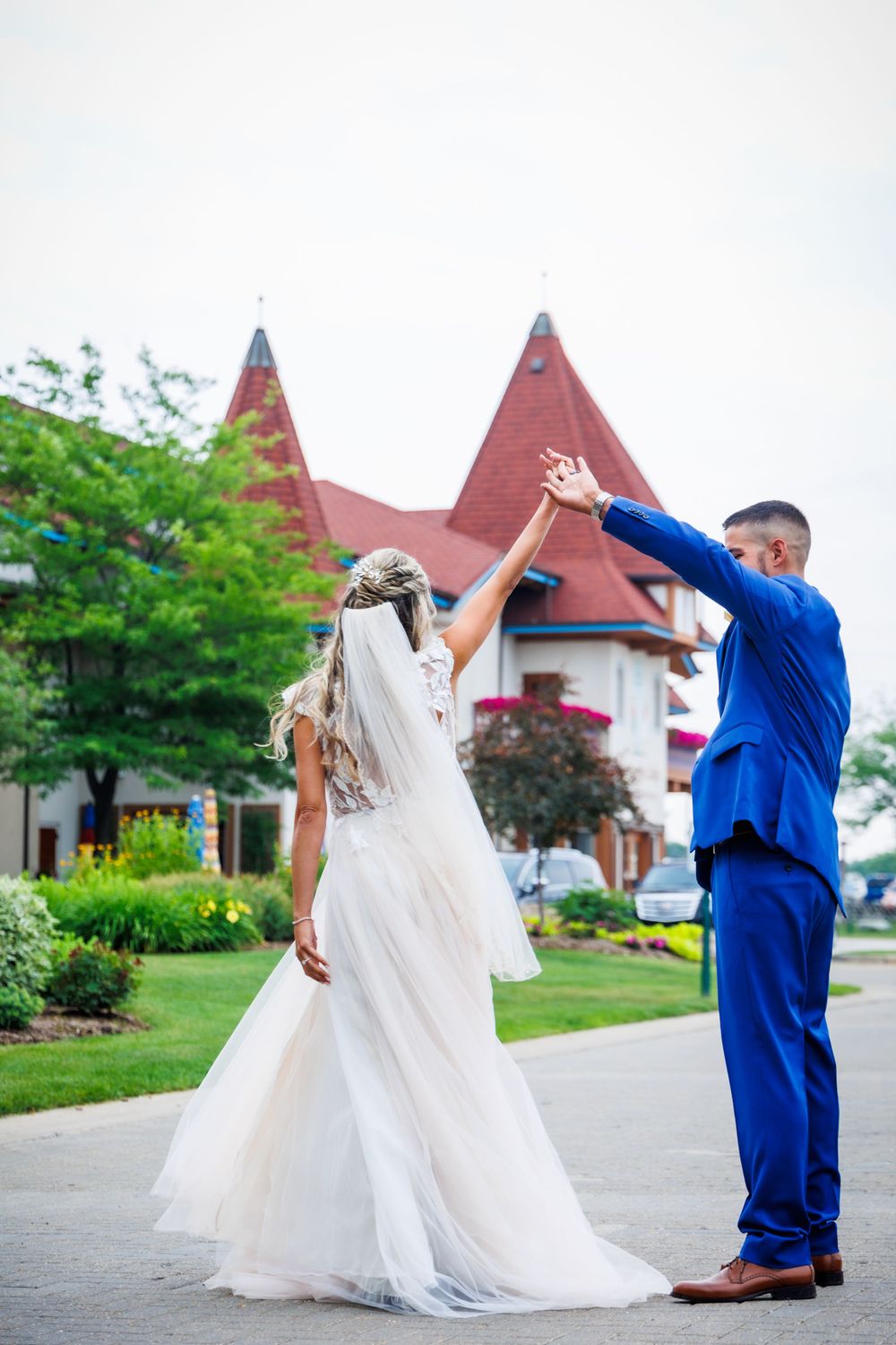 A newlywed couple dances joyfully outside a building with red spires.