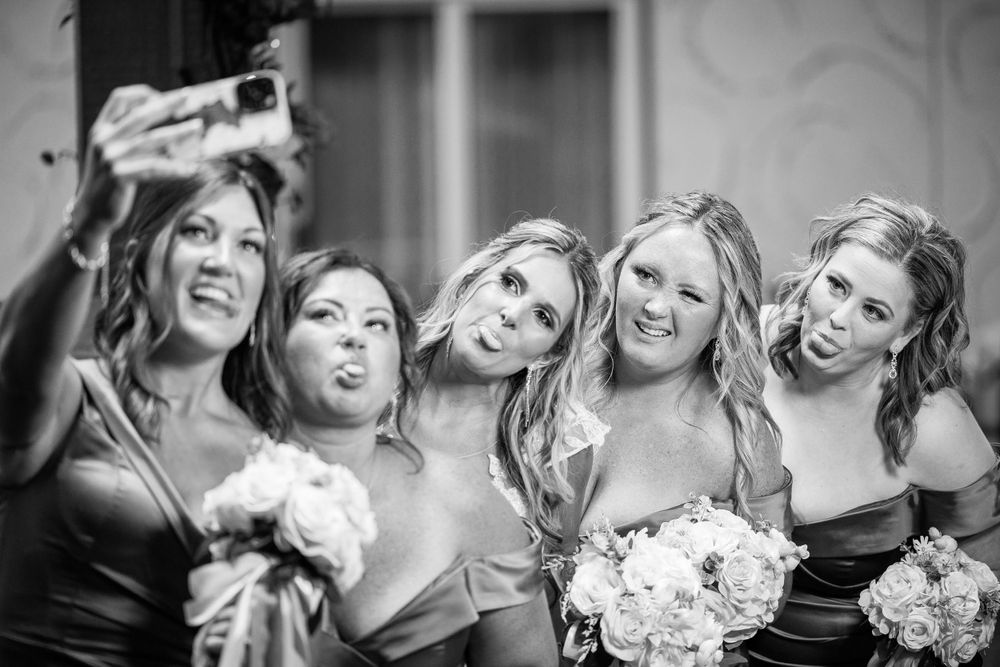 Fun candid moment of bridesmaids making silly faces for a black and white photo.
