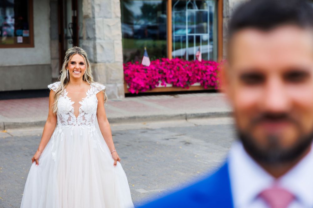 A bride in a white lace dress poses behind her groom wearing a vibrant blue suit.
