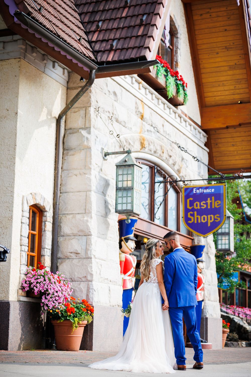 Wedding couple stands beneath Castle Shops sign with colorful flowers and stone architecture.