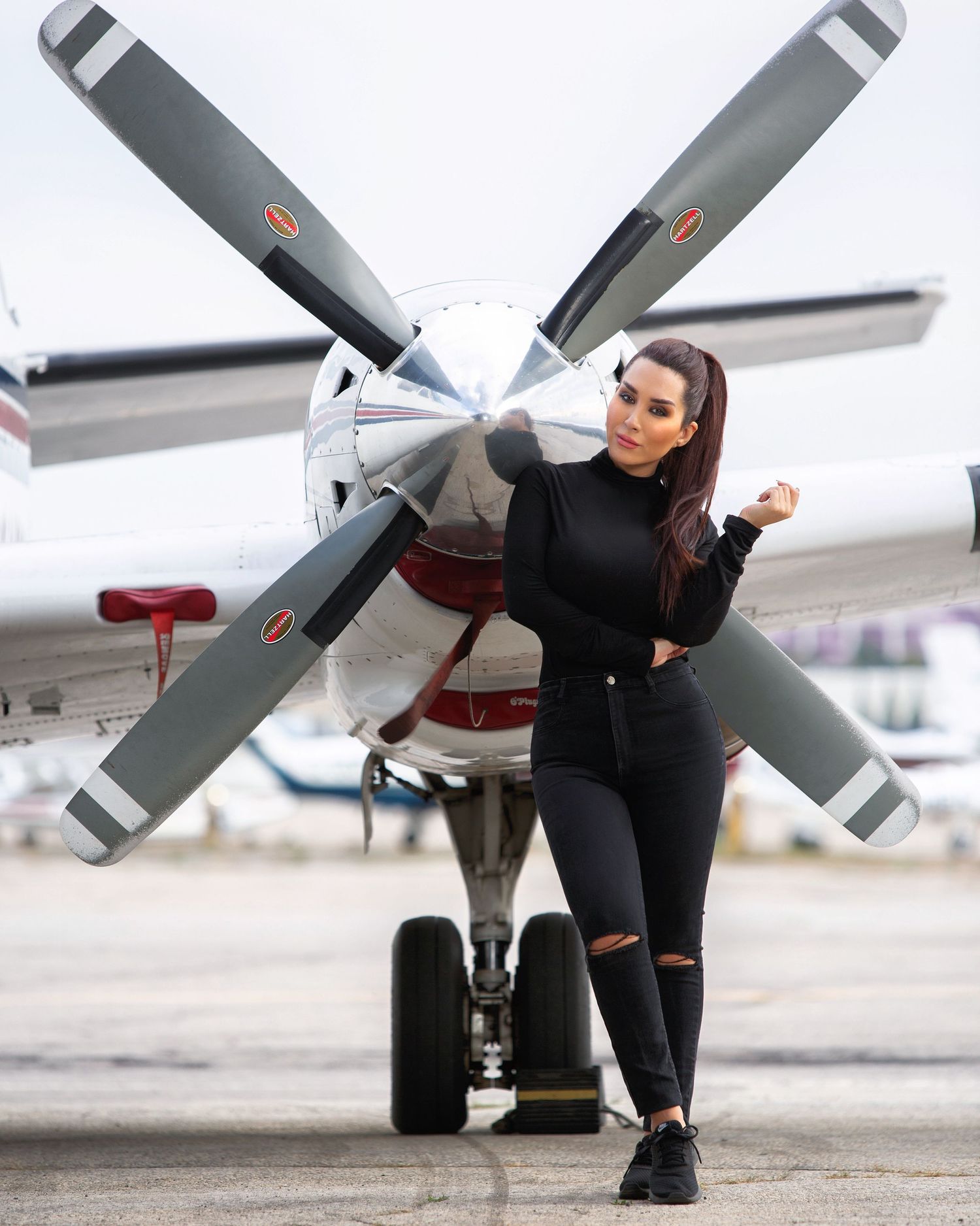 A woman in black attire poses with an aircraft on a runway, showcasing different angles and perspectives.