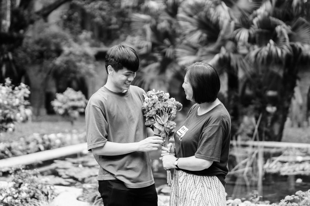 A black and white photo of a couple sharing flowers in a garden.