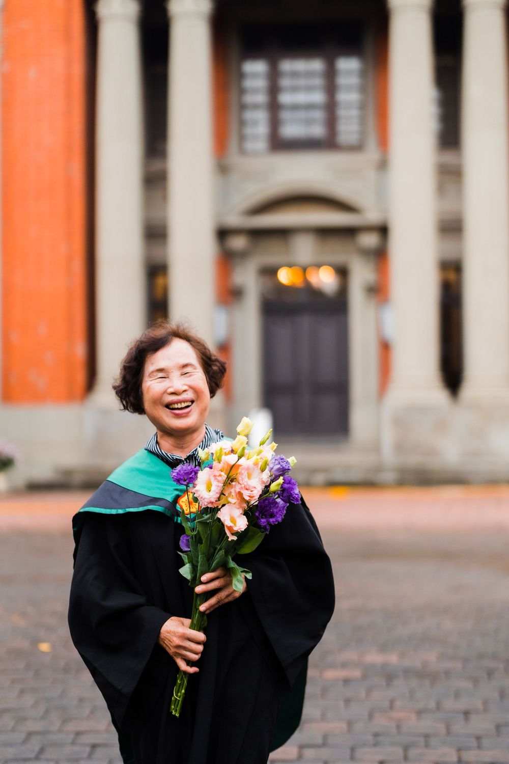 Graduate holding colorful bouquet while posing in front of historic university building.
