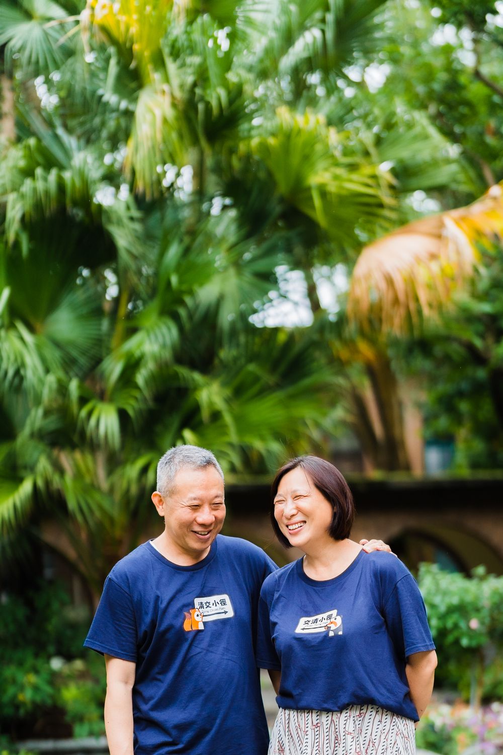 A couple in matching navy blue t-shirts smiles together in a lush garden.