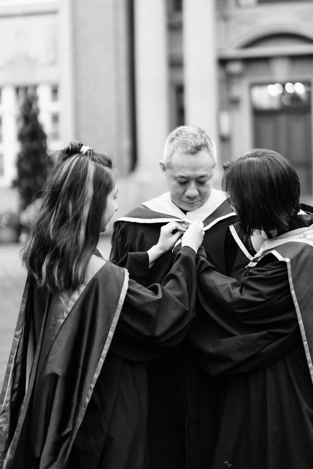 Graduates in black robes gather for a candid moment during commencement at a stately campus building.