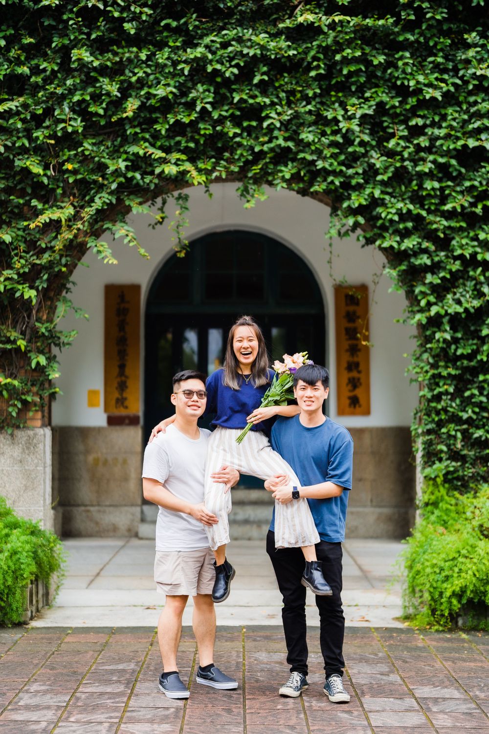Three people gather under an ivy-covered archway with flowers.