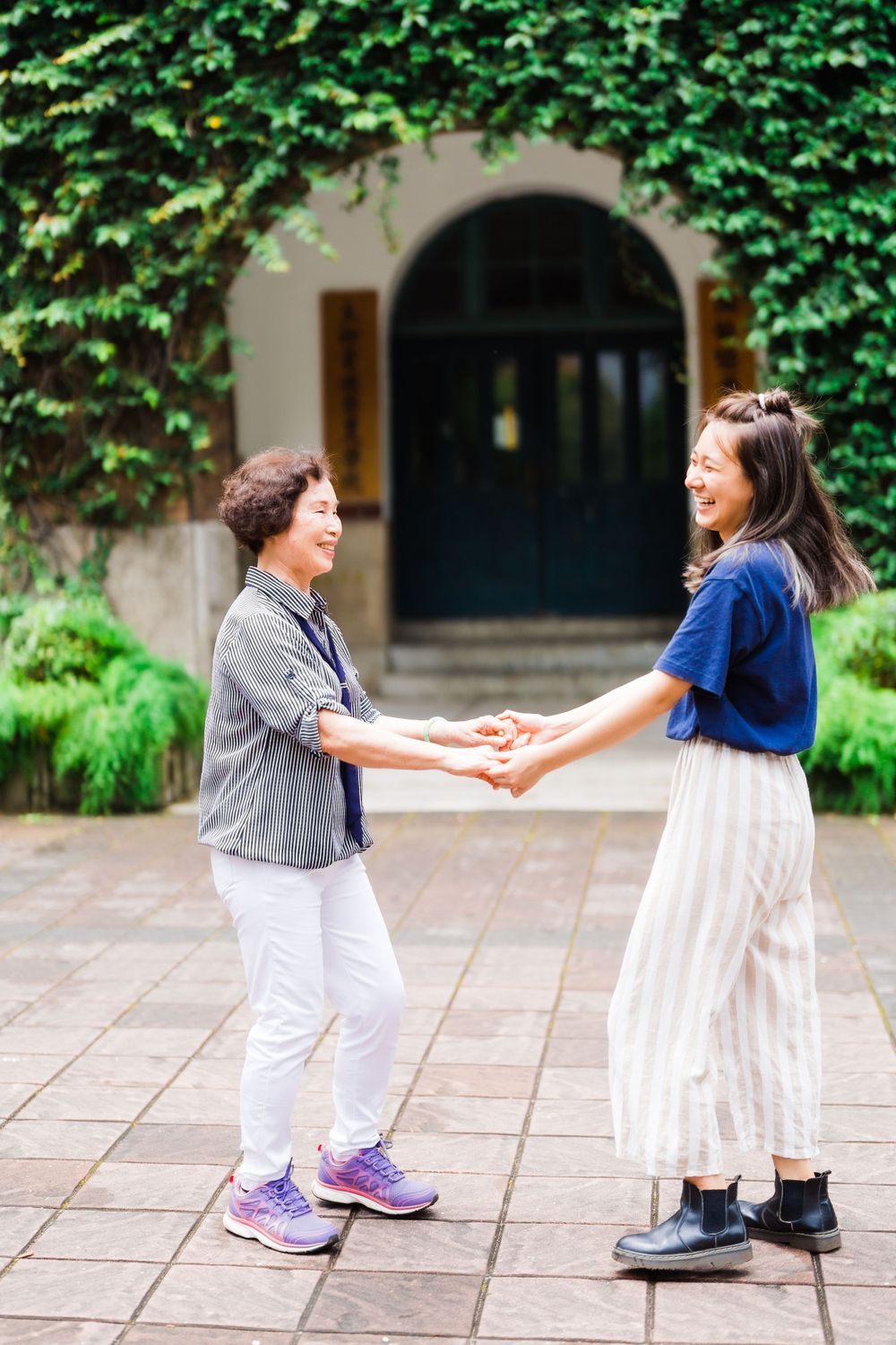 Two people hold hands and share a happy moment in a garden courtyard.