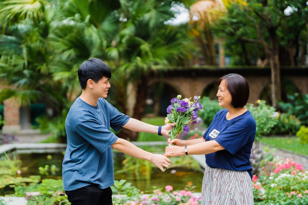A couple shares a tender moment exchanging flowers in a lush garden with palm trees.