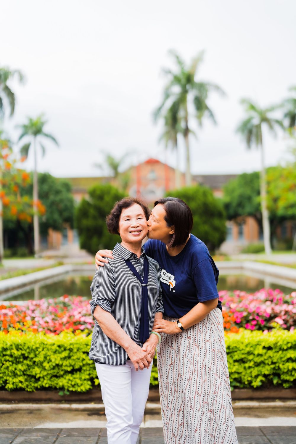 Two people embracing and laughing in a garden with palm trees and flowers.