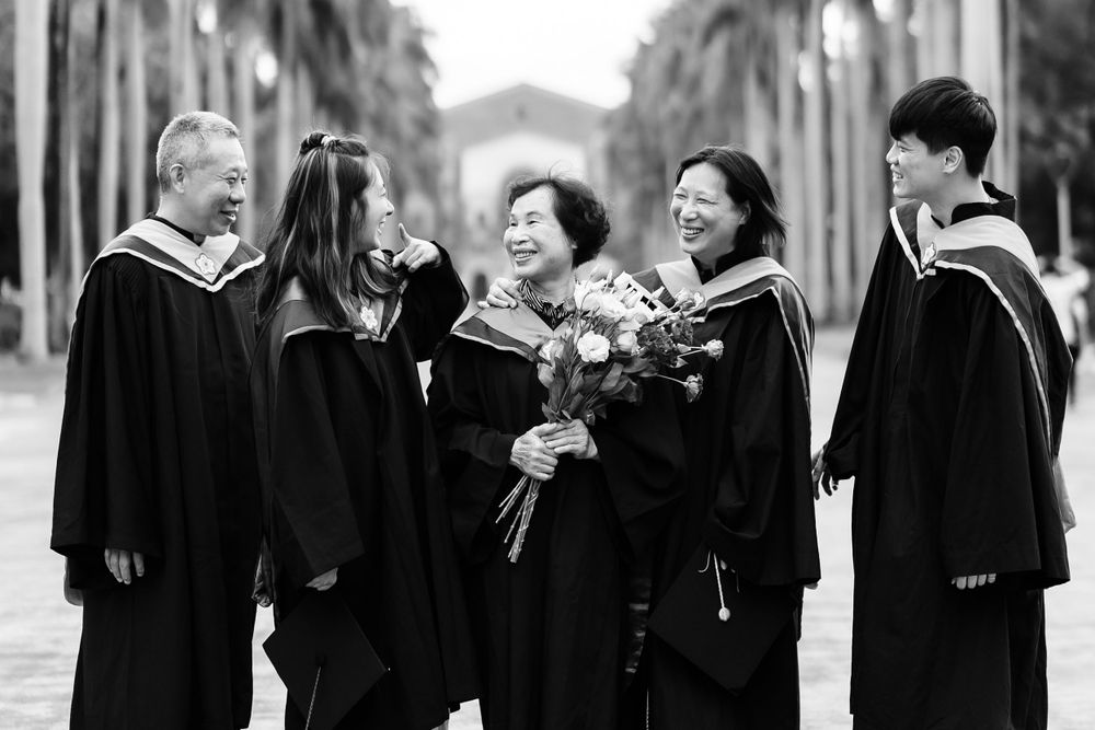 Black and white graduation photo showing group in academic regalia holding bouquet.
