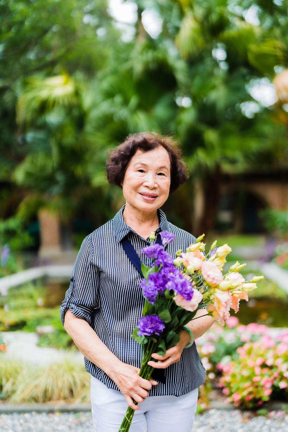 Someone holding purple and yellow flowers poses in a peaceful garden setting.
