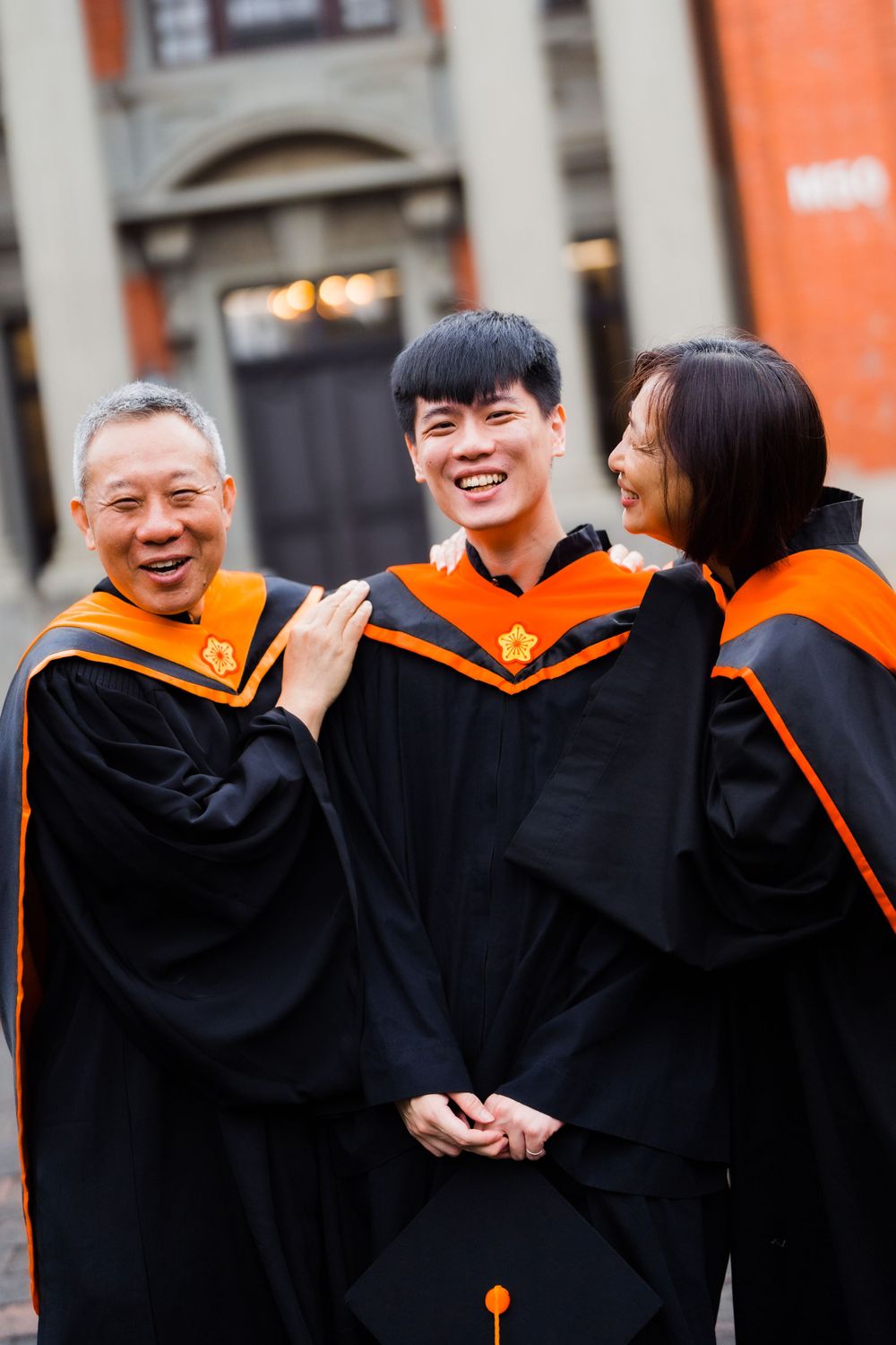 Graduates wearing black and orange academic regalia share a joyful moment during commencement.