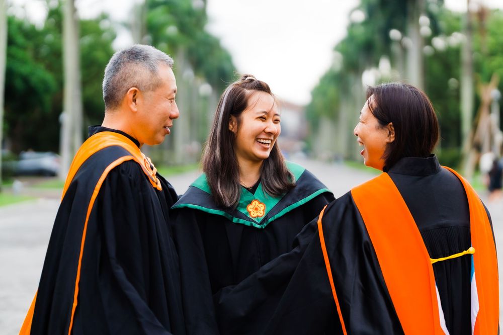Joyful graduation moment shared between faculty and graduate on palm-lined walkway.