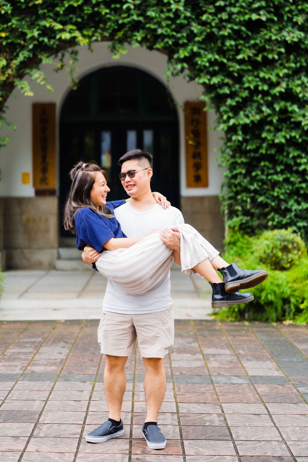 A playful couple poses in front of an archway with one person carrying the other.