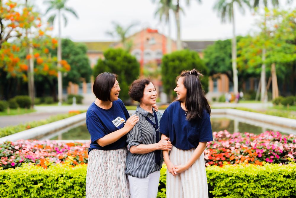 Friends share joyful laughter while standing in front of a garden with palm trees and flowers.