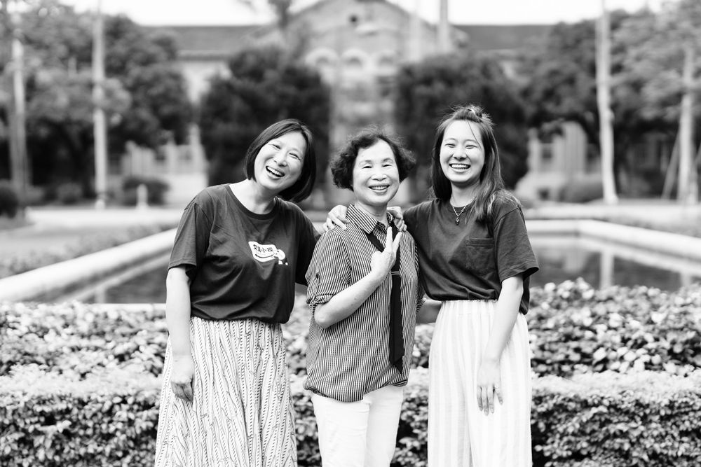 Black and white photo of three people laughing together in a garden setting.