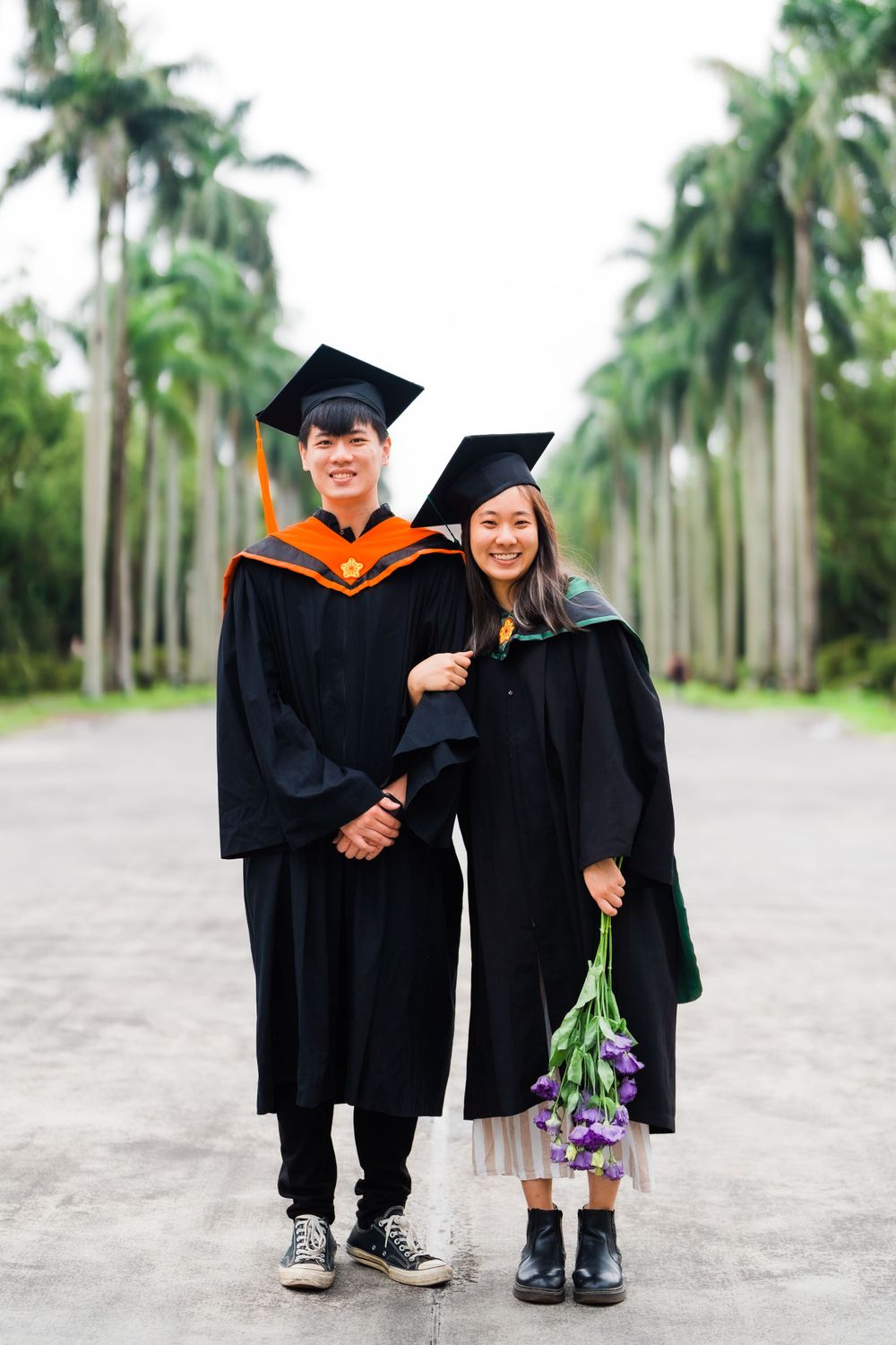 Graduates in academic regalia stand together on a palm-lined walkway during their graduation photoshoot.